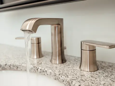 Brushed nickel bathroom faucet with running water on a granite countertop in a luxury Cincinnati, Ohio home by Frazier Homes.