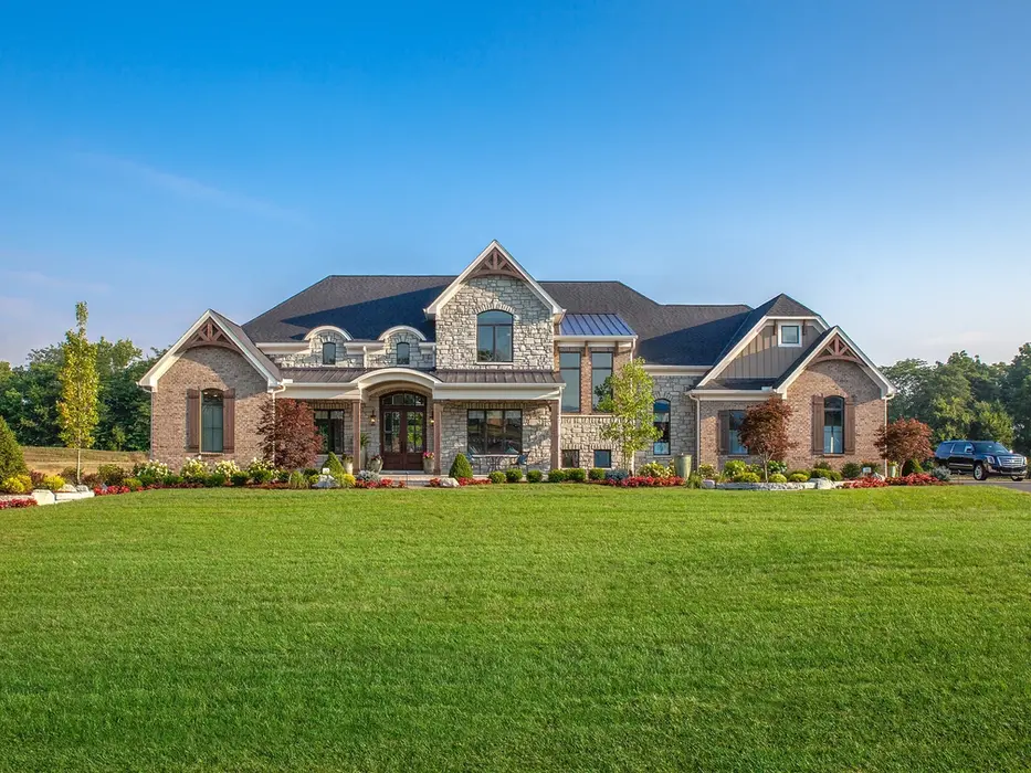 Luxury custom home exterior in Lebanon, Ohio featuring stone and brick architecture, lush landscaping, and expansive front lawn by Frazier Homes.