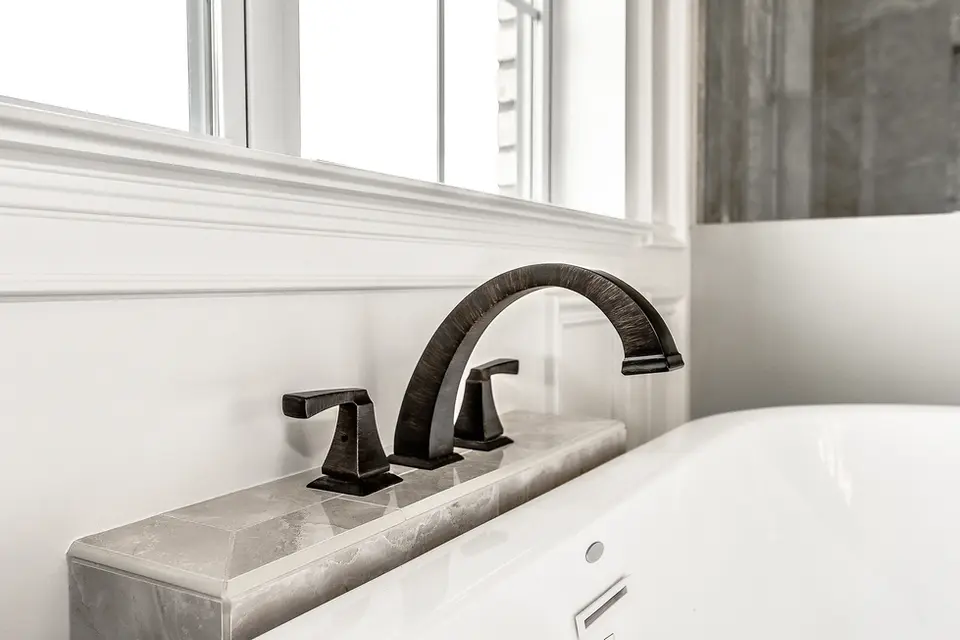 Close-up of oil-rubbed bronze freestanding tub faucet in a Liberty Township, Ohio luxury custom home featuring marble surround, white trim detailing, and spa-style master bathroom design by Frazier Homes.