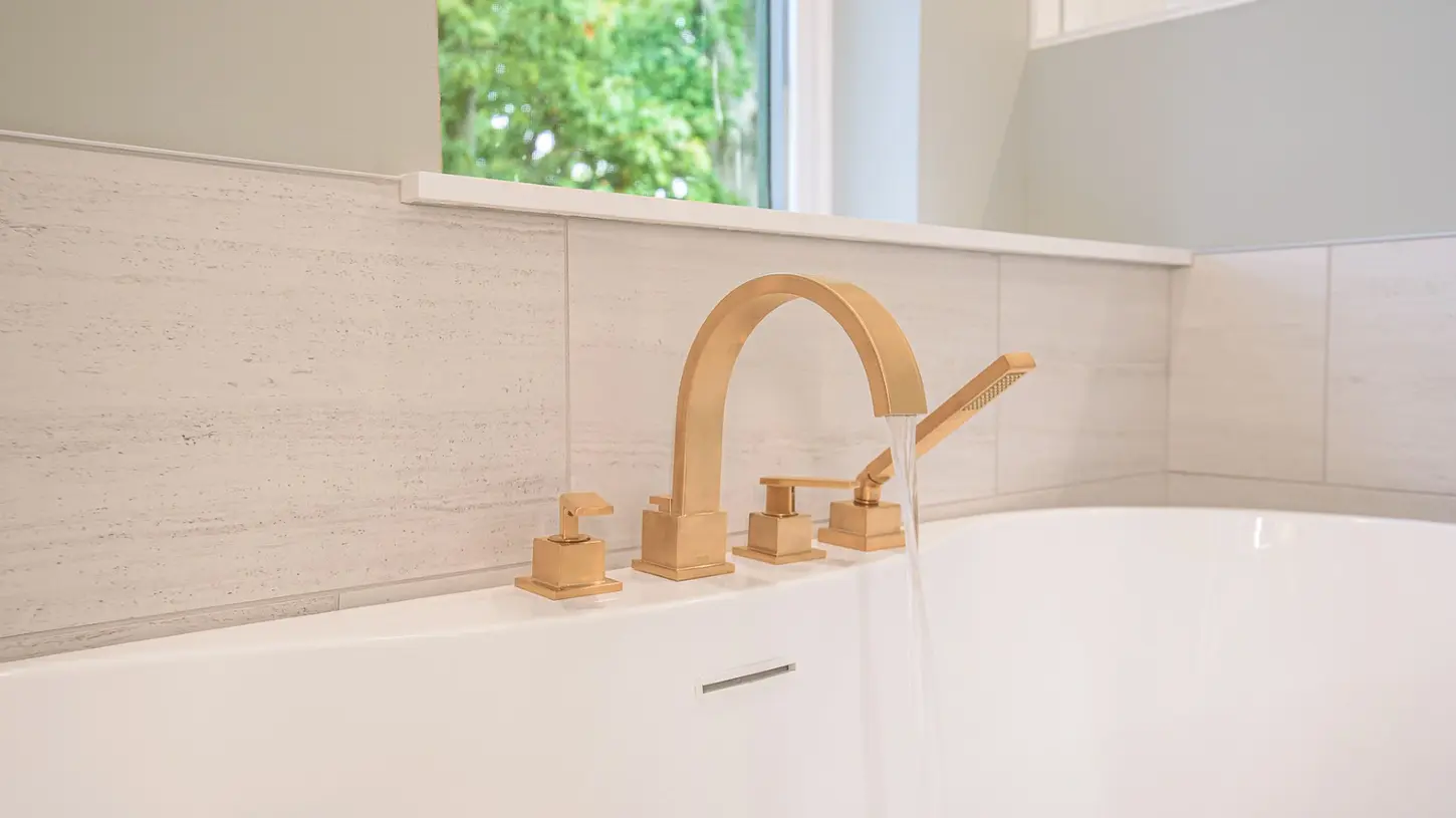 Brushed gold tub faucet filling a white freestanding bathtub in a Hyde Park master bathroom by Frazier Homes in Cincinnati, Ohio.