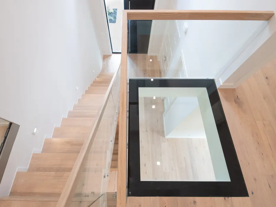 Modern custom staircase in Montgomery, Ohio featuring light oak stairs, glass railing, and black-framed glass floor landing by Frazier Homes.