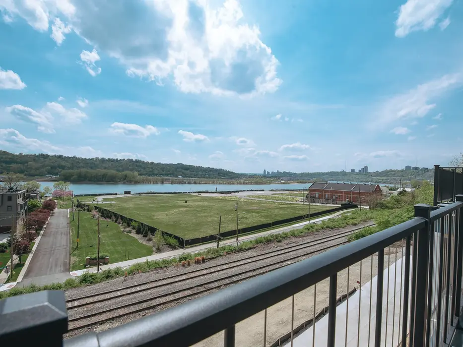 Panoramic river and valley view from a private balcony at Walworth Junction in Columbia Tusculum overlooking green space, rail lines, and the distant Cincinnati skyline.
