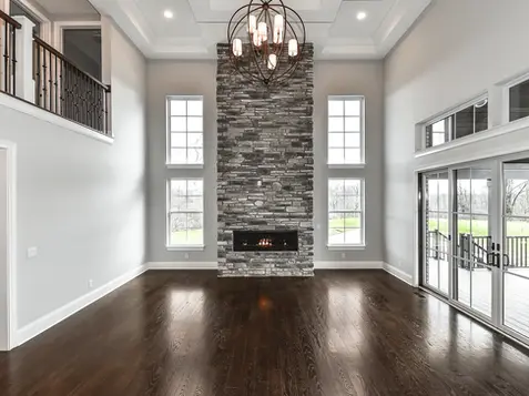 Luxury Liberty Township living room built by Frazier Homes with tall windows, dark hardwood floors, stone fireplace, custom ceiling lighting, and large sliding glass doors.