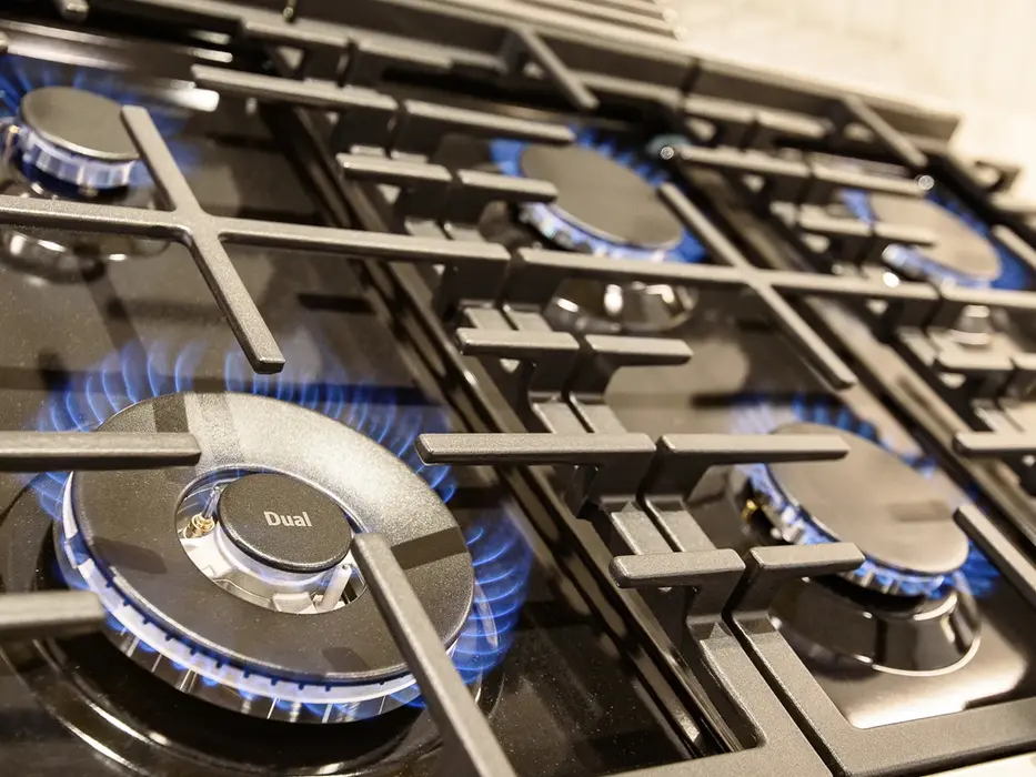 Professional gas cooktop with blue flames and cast iron grates in a Montgomery Ohio luxury kitchen remodel by Frazier Homes.