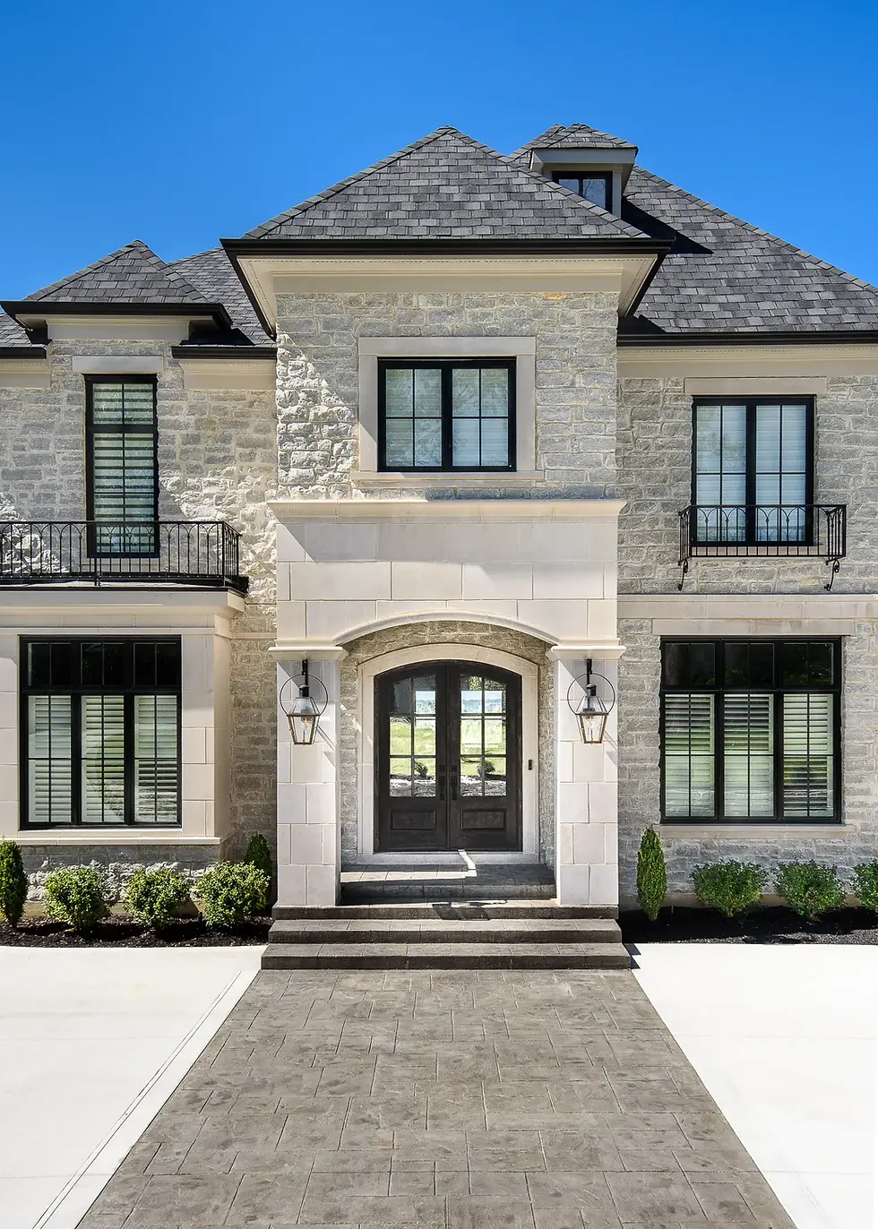 Luxury custom home exterior in Hyde Park, Cincinnati, featuring natural stone, black-framed windows, an arched entry, and refined architectural details.