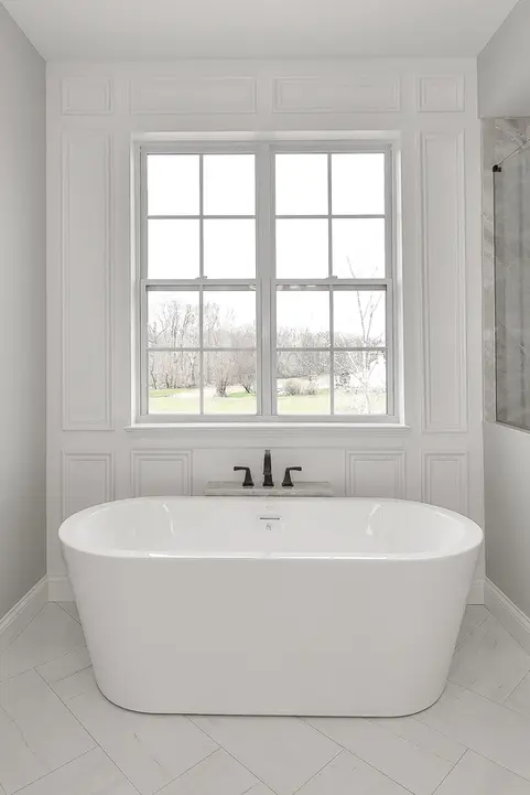 Freestanding soaking tub in a Liberty Township, Ohio luxury custom home featuring paneled accent wall, large window with natural light, marble tile flooring, and spa-style master bathroom design by Frazier Homes.