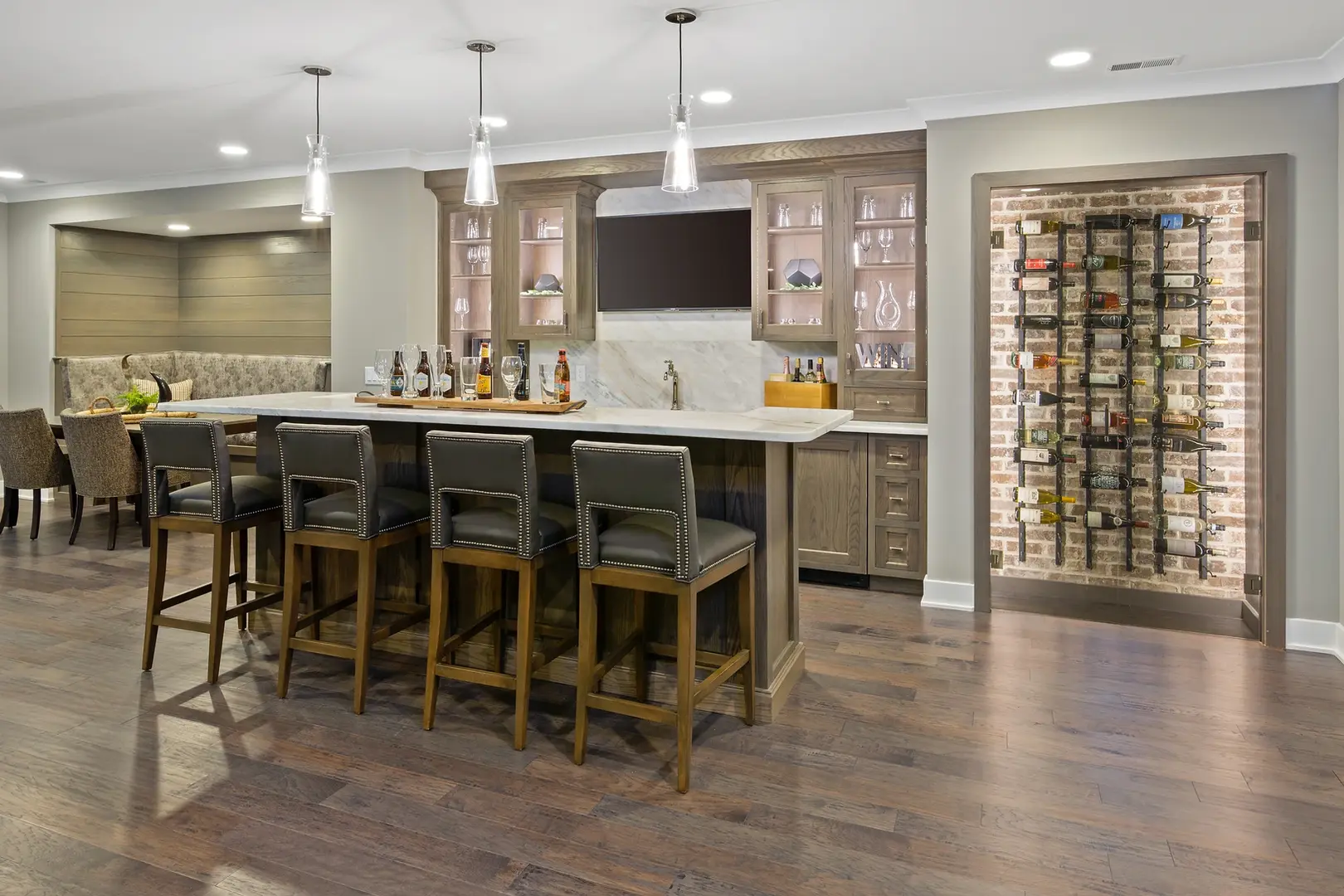 Luxury custom bar area with marble backsplash, illuminated cabinetry, seating island, and a brick wine wall designed by Frazier Homes.