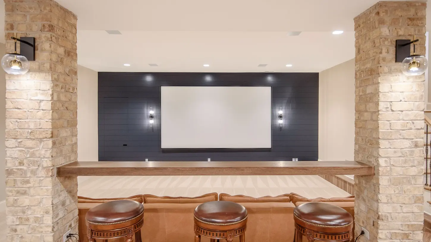 Luxury flex room home theater with brick columns, navy shiplap feature wall, large projector screen, raised bar seating, and custom design by Frazier Homes in Cincinnati, Ohio.