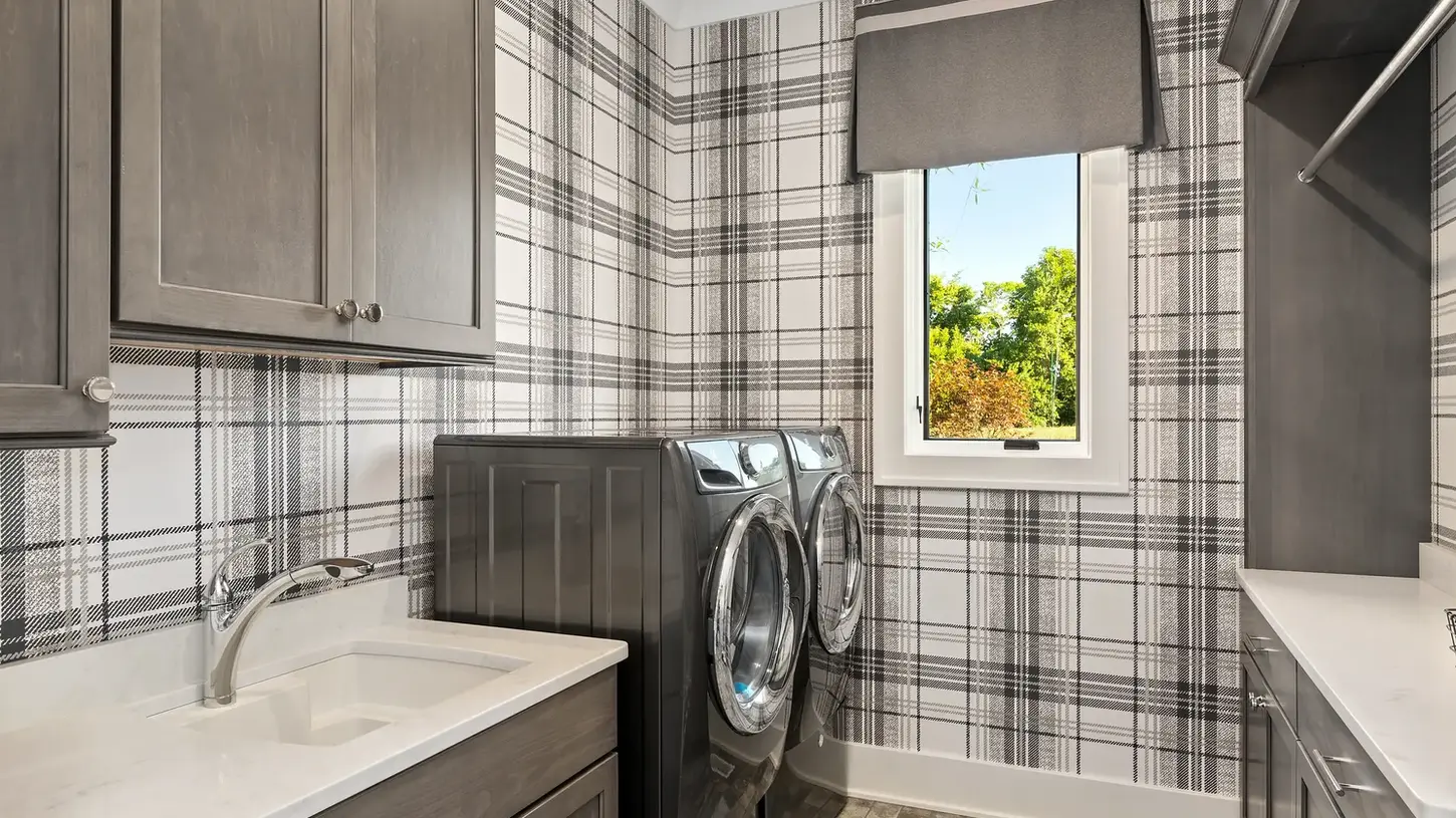 Luxury laundry room in Lebanon, Ohio with plaid wallpaper, custom gray cabinetry, quartz counters, and front-loading appliances.