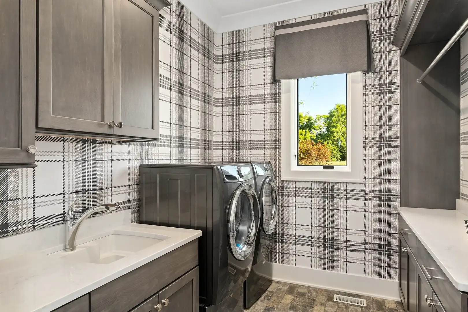Luxury laundry room in Lebanon, Ohio with plaid wallpaper, custom gray cabinetry, quartz counters, and front-loading appliances.