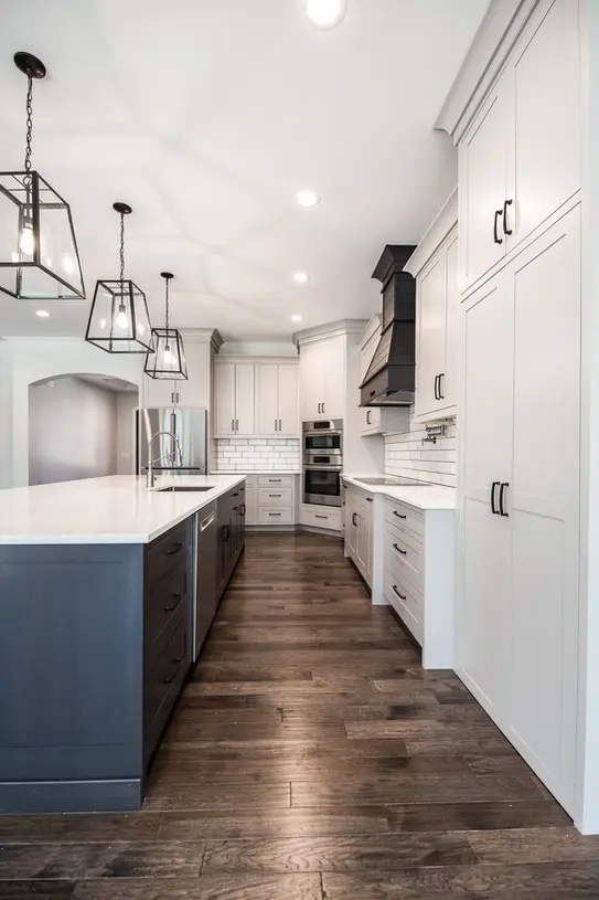 Two-tone custom kitchen with navy island, white cabinets, lantern pendant lighting, hardwood floors, and luxury finishes.