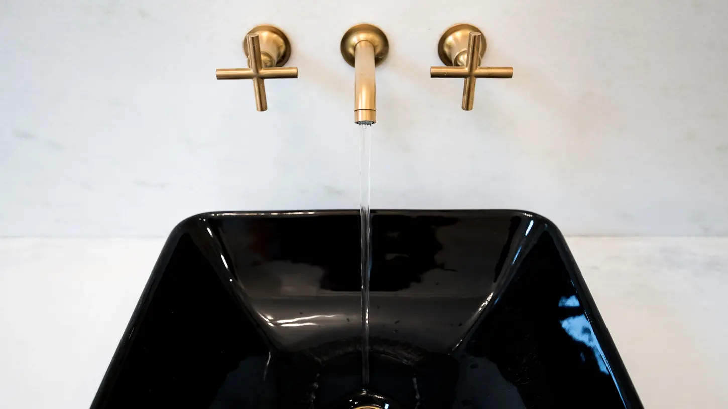 Black vessel sink with brushed gold wall-mounted cross-handle faucets and a modern minimalist backsplash in a luxury Frazier Homes Walworth Junction bathroom.