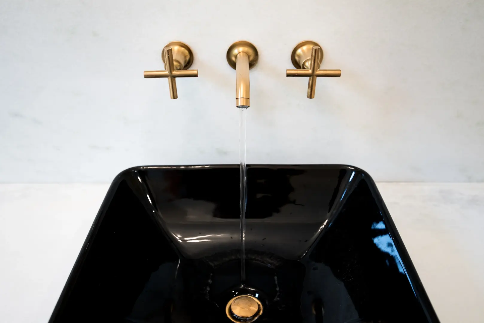 Black vessel sink with brushed gold wall-mounted cross-handle faucets and a modern minimalist backsplash in a luxury Frazier Homes Walworth Junction bathroom.