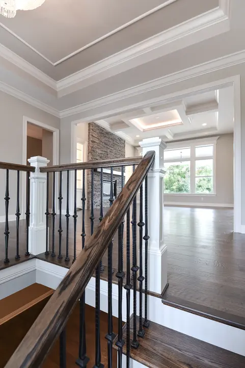Luxury Liberty Township custom home interior featuring wood staircase with black iron balusters, detailed crown molding, coffered ceiling, stone fireplace, and open-concept living space by Frazier Homes.