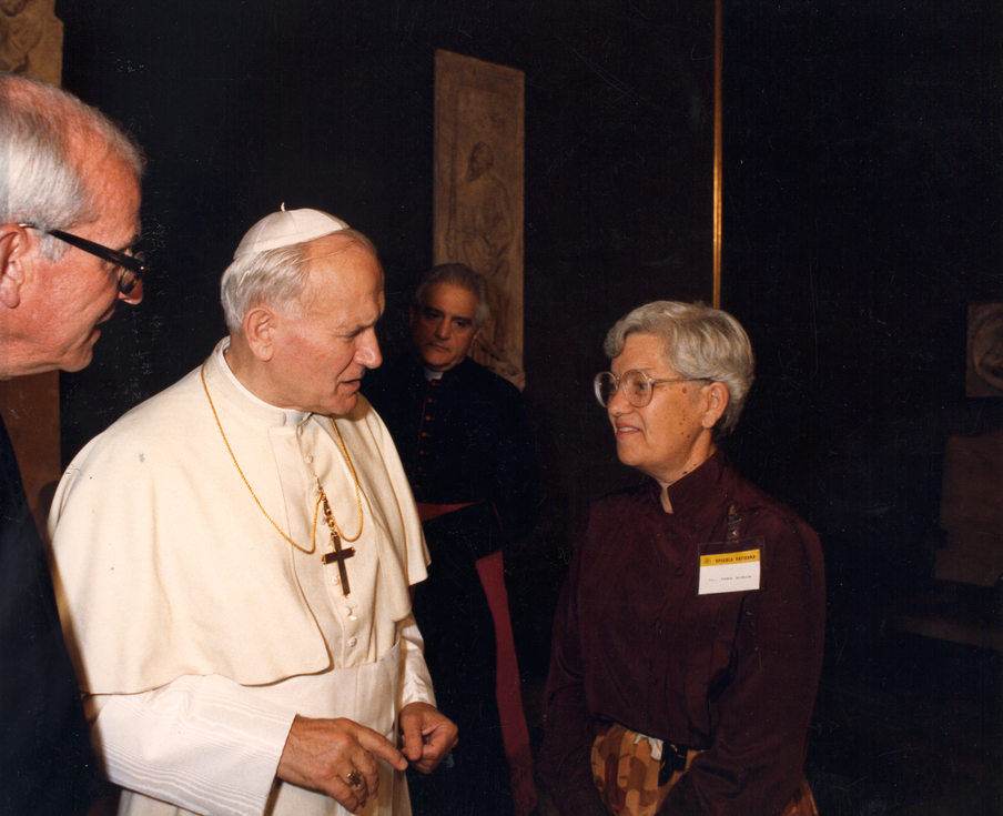 Dr. Rubin is standing on the right in a dark brown shirt and turtleneck speaking with Pope John Paul II on the left.