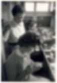 Dr. Rita Levi-Montalcini stands at a lab bench behind two young women. The two young women hold lab samples, and Dr. Levi-Montalcini is supervising them.