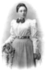 Photo of Emmy standing. Her hand rests on a chair in front of her.