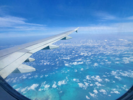 An airplane wing as seen from the window of the airplane, with scattered clouds and aqua and blue water below