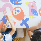 Two children painting colorful shapes on a white table from above