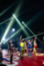 Group of performers raising hands under bright stage lights at a show.