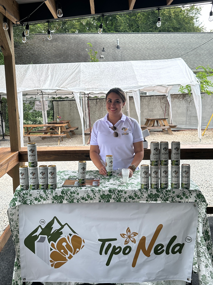 Woman stands behind Tipo Nela display; with Tipo Nela cans