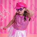 Young girl in pink outfit poses with pink background, wearing sunglasses