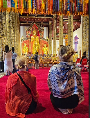 Two people facing a golden Buddha statue in a Thai temple