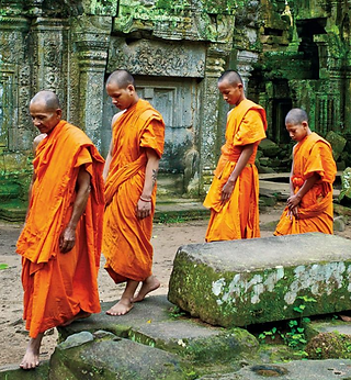 Four monks in orange robes walk through ancient ruins