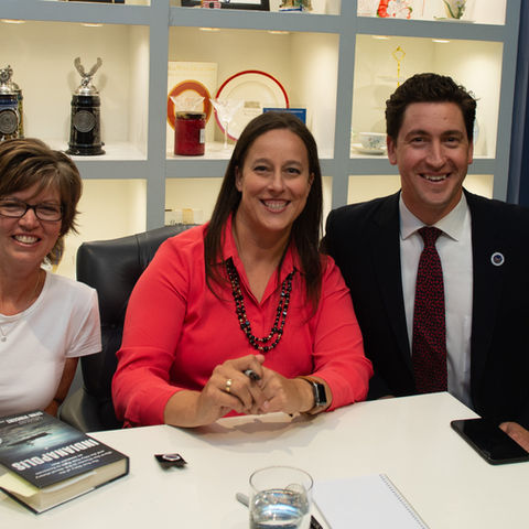 Three smiling people including Sara Vladic with the INDIANAPOLIS book at the table