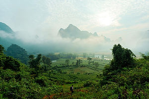 Green valley and mountains surrounded by fog on a sunny day