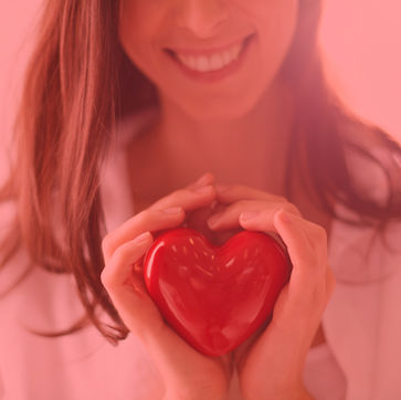 Smiling woman holding a red heart, showing love and care with her hands.