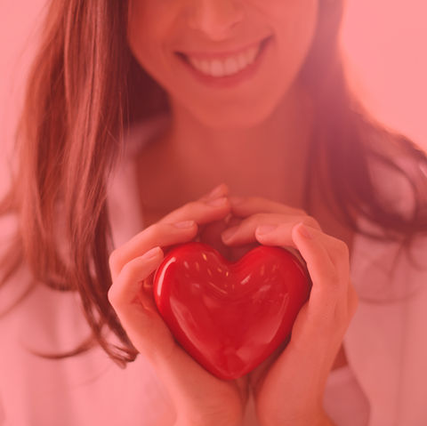 Smiling woman holding a red heart, showing love and care with her hands.