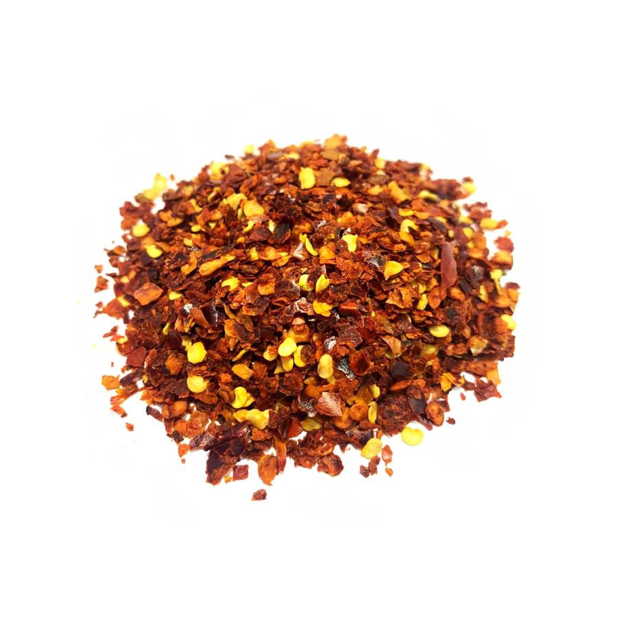 Подрібнений червоний перець чілі з насінням, яскрава гостра спеція, розсипана на білому фоні