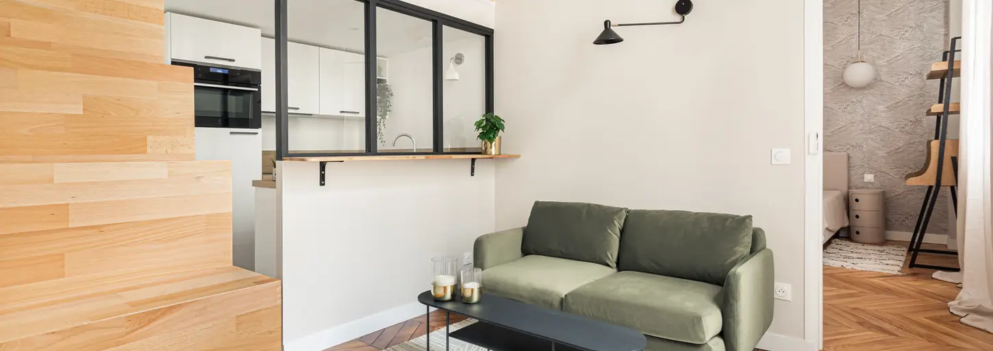 Petit appartement 2 pièces à Paris aménagé avec une mezzanine ouverte sur le salon. Le canapé est de couleur kaki et le décor minimaliste.