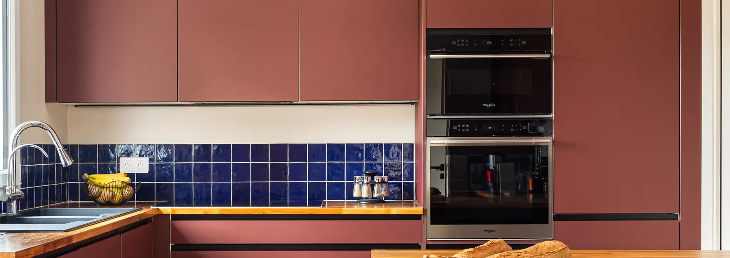Une cuisine aménagée en L avec un îlot central de couleur terracotta. Les éléments de la cuisine sont de couleur terracotta et la crédence de couleur bleu roi.