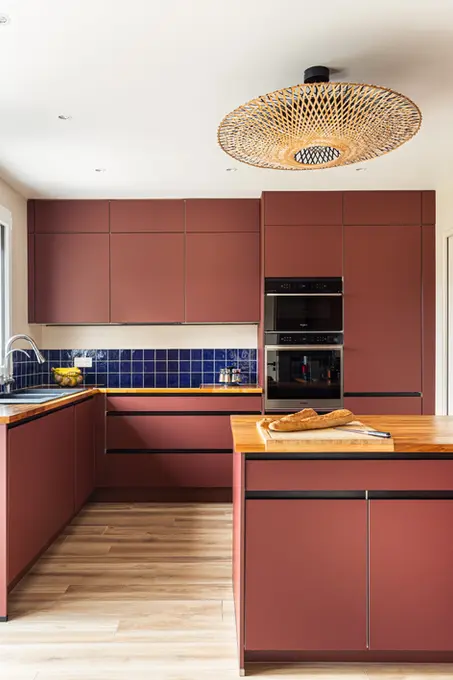 Une cuisine aménagée en L avec un îlot central de couleur terracotta. Les éléments de la cuisine sont de couleur terracotta et la crédence de couleur bleu roi.