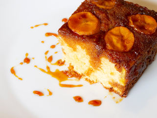 Slice of banana cake topped with caramelized bananas and caramel sauce on a white plate