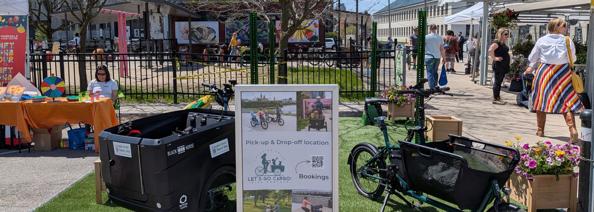 An area with astroturf, cargo bikes and market activity all around.