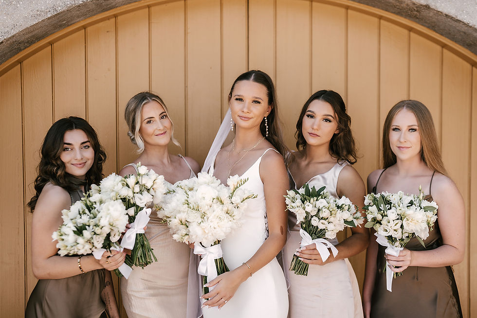 The bride and her bridesmaids. Bridemaids have on neutral colored dresses. Bouquets are simple and beautiful white flowers.