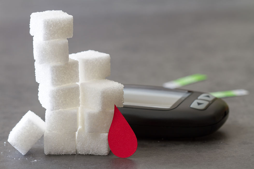 Sugar cubes stacked beside a glucose metre and red blood drop, symbolizing diabetes on a gray tabletop.