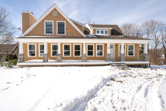 Exterior view of a tan house with windows, snow, and a porch.