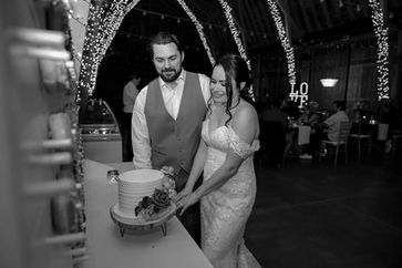 Newlyweds cut their cake beneath Windmill Winery's fairy-lit cathedral barn arches, the glowing LOVE marquee setting the scene in timeless black and white.