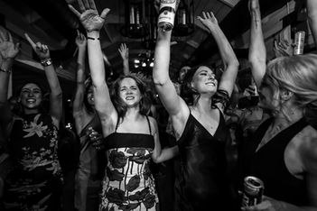Guests raise their beers in joyful celebration on Windmill Winery's dance floor, captured in black and white at peak reception energy.