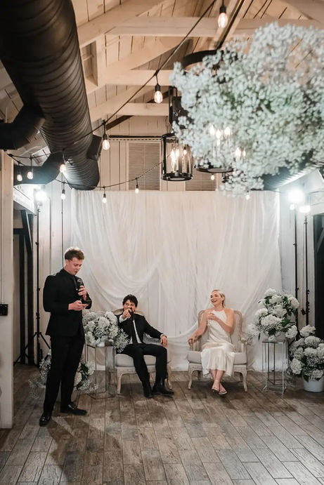 Groom's belly laugh during the best man's toast at Windmill Winery, framed by cascading white florals and candlelit ambiance with bride beside him.