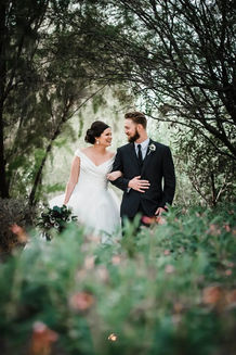 Bride and groom walk arm-in-arm down a romantic tree-lined garden pathway at Windmill Winery, with soft daylight and botanical framing.