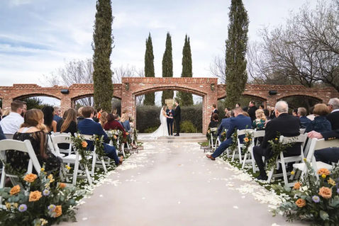 Petal-strewn aisle leads guests toward the brick aqueduct ceremony arch at Windmill Winery, orange and yellow rose florals lining every white folding chair.