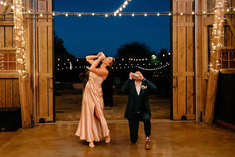 A wedding party shotski under twilight string lights at Windmill Winery's open barn doors, the grand-entrance moment captured in pure candid celebration.