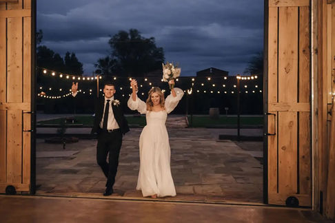 Bride and groom walk arm in arm down the brick pathway at Windmill Winery, guests lining both sides and cheering their grand entrance to the reception.