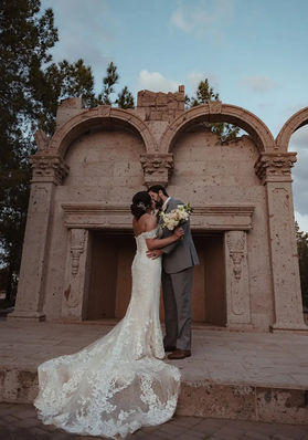 Couple shares a quiet kiss at the towering travertine folly arches at Windmill Winery, lace cathedral train cascading down the limestone steps at twilight.