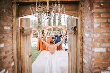 Bride throws her arms wide as she bursts through Windmill Winery's iconic barn doors, the wedding party erupting in cheers along the brick aqueduct path.